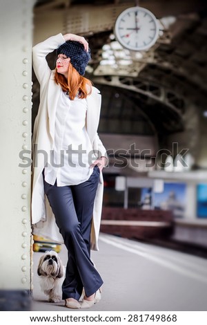 Elegant ginger hair woman and shih tzu dog on the platform under the clock waiting train at the Vitebsk railway station. Image with selective focus