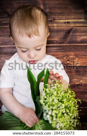 Adorable little boy in green trousers with fair hair and bunch of lilies of the valley
