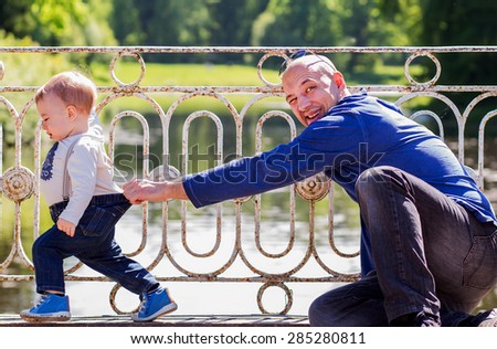 Handsome bold father on a bridge has caught by trousers his little son who is trying to run away