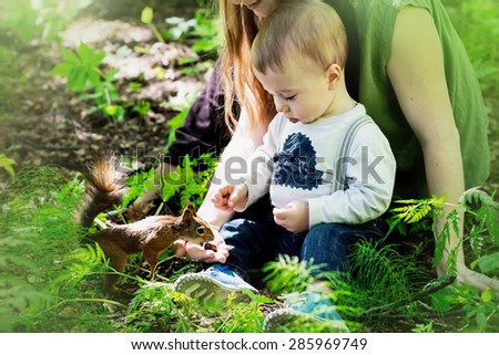 Redhaired mother and her  little son are feeding squirrel