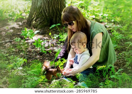 Redhaired mother and her cute little son with fair hair are feeding squirrel from hand