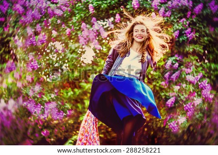 Sunny dandelion. Wind has caught sunset sun in hair and peering under the skirt in passing. Beautiful young woman in windy lilac garden at the sunset