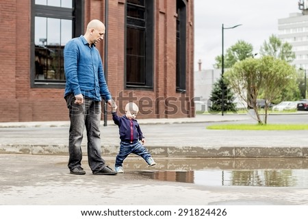 Handsome man with his little cute son are walking. Little boy is playing tricks by tramping along the border. Father is holding him. They both are having fun. Image with selective focus