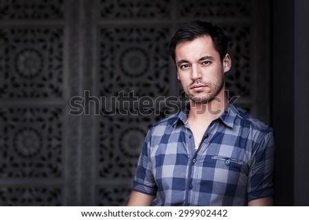Portrait of gorgeous dark-haired young man against an oriental patterned wall background. Image with selective focus