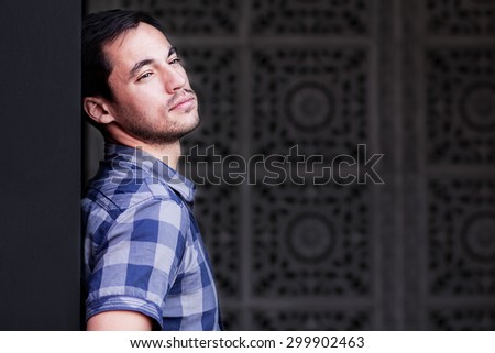 Portrait of dark-haired young man against an oriental patterned wall background. Image with selective focus