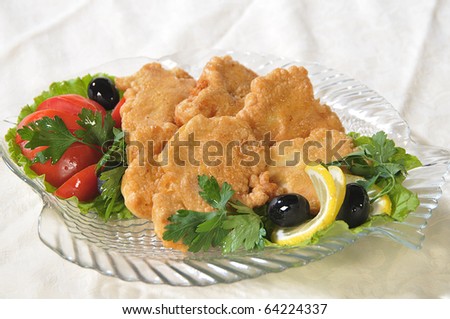 Pieces of fish filet are fried in an egg and decorated a tomato, greenery and olives