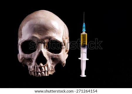 Skull and syringe of yellowish liquid . The syringe is filled with medicine , poison or drugs. Isolated on black
