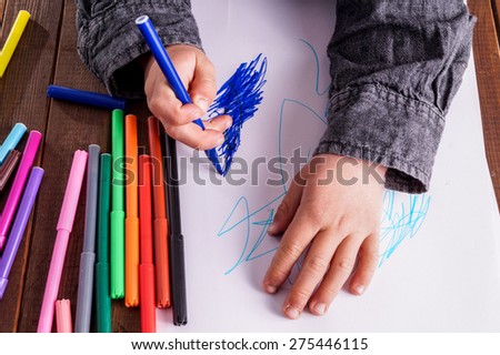 Little boy draws a drawing. He has many markers and are very focused on what he is doing