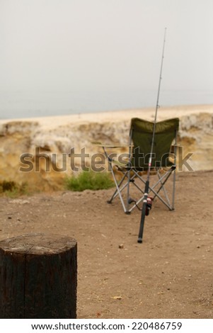 Fisherman\'s chair and fishing rod sitting by ocean break wall at the beach.