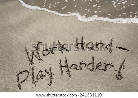 Work hard, play harder, a message written in the sand at the beach.