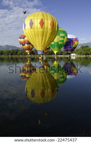 Hot air balloons flying at water level over lake.