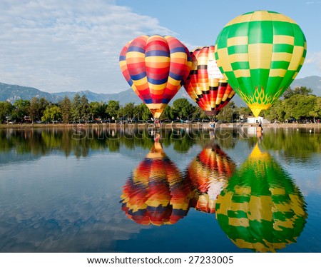 Trio of hot air balloons flying low over water with a beautiful reflection.