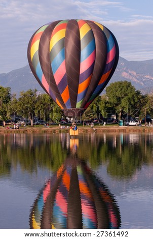 Single hot air balloon flying low over water with a nice reflection.