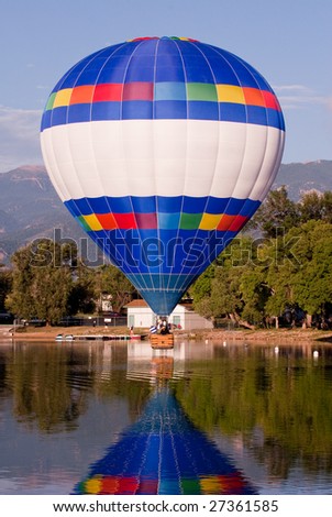Single hot air balloon flying low over water.