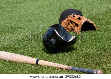 Baseball bat, glove and batting helmet lying on the field.