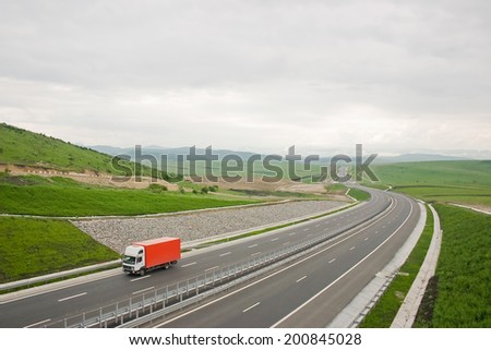 Red truck on a highway in a hilly area.