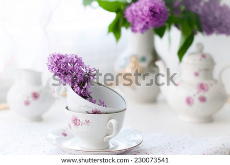white tea set, a bouquet of lilac in a vase and a sprig of lilac in a cup. selective focus