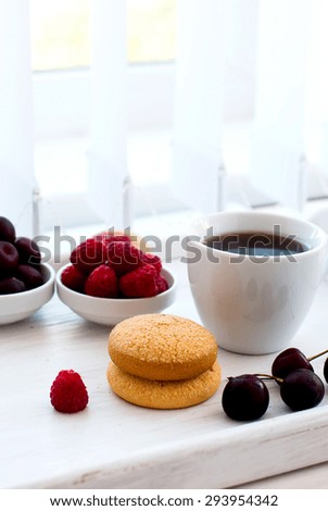 cup of black strong coffee and two biscuits with berries - raspberries and cherries, summer light breakfast