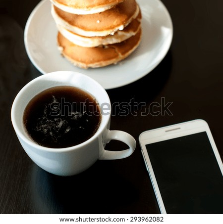 cell phone and a cup of black coffee and strong Pancake breakfast on black table