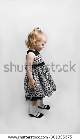 Girl in black and white dress stands and looks down into the profile
