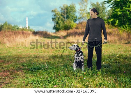 Young attractive man walking with an active dog Dalmatian on nature