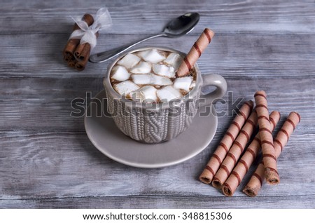 On a light background wooden table sweet drink and dessert cup and saucer with hot chocolate, marshmallow pieces, cinnamon, wafer rolls