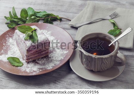 On the green blue background wooden table plate with a piece of the pie dish pie and a cup of tea and mint leaves and twigs -  Art reception toning photo