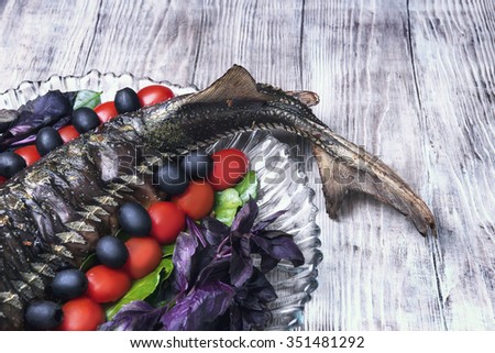 On a light wooden background vintage style with a celebratory dinner baked fish sturgeon on a large glass dish decorated with lime leaves, olives, cherry tomatoes, basil