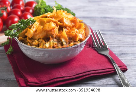 On a light wooden background in vintage style food dinner plate with Bolognese Tagliatelle pasta, cherry tomatoes on a branch, fork, napkin, towel red, green curly parsley