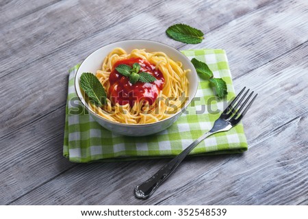 On a light wooden table dinner - in a plate of spaghetti with red tomato sauce, mint leaves