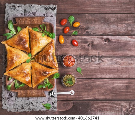 Delicious deep fried south Indian Samosa pies with meat, lettuce, mint chutney and tomato sauce on a wooden background in rustic style, empty place for text, top view
