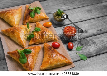 Delicious deep fried south Indian Samosa pies with meat, lettuce, mint chutney and tomato sauce on a gray wooden background in rustic style, empty place for text, recipe