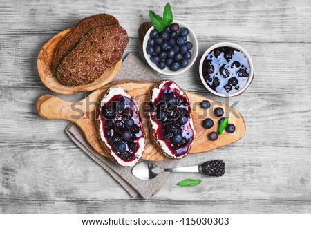 Sweet berry crostini sandwiches with blackberry jam and berries blueberries, whole grain bread for sandwiches, sandwiches board, spoon, mint leaves on a bright white background wooden, top view