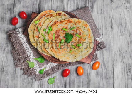 Stack of not sweet frying flour Flatbread Paratha roti, tortillas, cherry tomatoes, lettuce, napkin of burlap with lace, wooden board served on a light white surface, top view