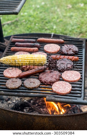 Grilling camping food (meat, sausages, burger and corn) outdoors
