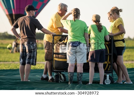 Iowa, United States - July 29, 2015: A team of hot air balloon crew members gathered near their balloon-holding cart. They were planning the best way to unpack their hot-air balloon.