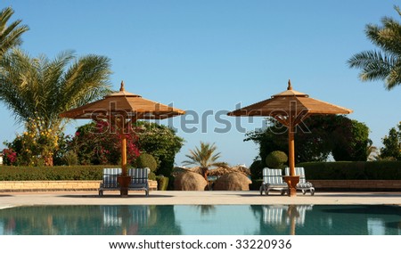 Two sunshades with chaise-longues and swimming-pool in hotel
