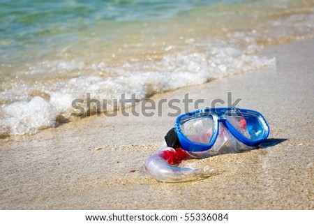 Mask and snorkel lying on sand of beach and washing by surf