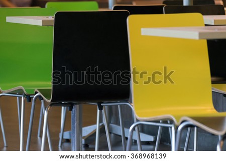 Interior of the restaurant fastfood with bright colored chairs and empty tables without visitors defocus on people background
