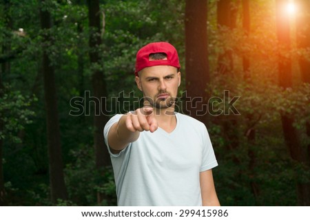 You can do it! serious young man pointing at camera and inspire while standing against green forest background. Sun shine light background.
