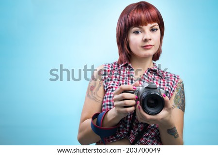 Attractive young female photographer with tattoos and film camera in blue gradient background