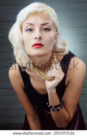 Portrait of blonde woman in trendy clothing holding neck chain