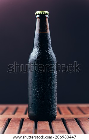 Dark beer in amber bottle on wood board table on dark purple background