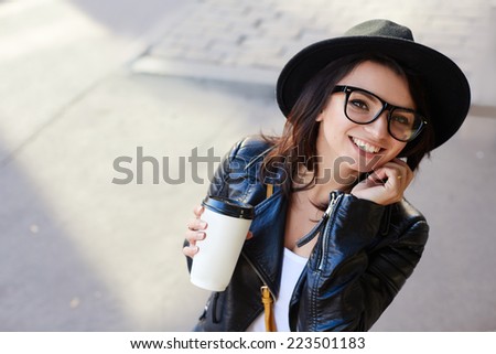 Beautiful girl with coffee smiling on the background of the street. Hipster style
