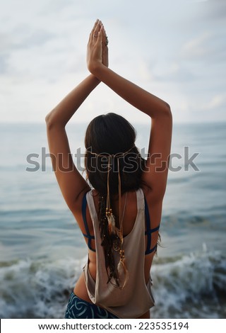 Beautiful girl hippie standing back and looking at the sea. Yoga and meeting the dawn. Tranquility and meditation.