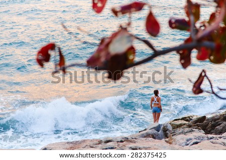 Beautiful girl walking on the rocks by the sea and watching the sunrise.