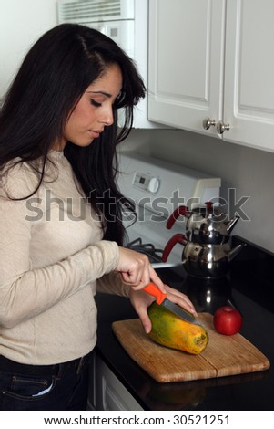 Young female at home in the kitchen, cutting fruits on cutting board
