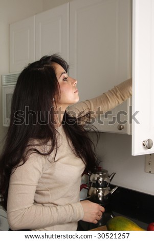 Young female at home in the kitchen, reaching food item from the cabinet
