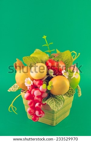 Bouquet of artificial fruits and leaves arrangement in vase on green background