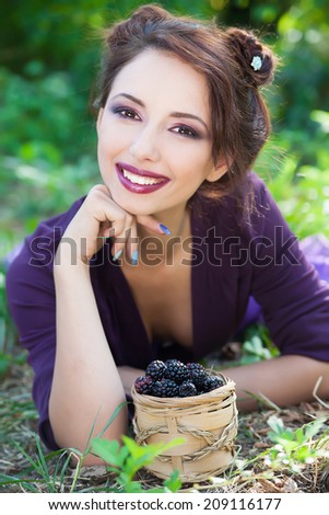 Portrait of beautiful smiling young brunette woman posing with basket of blackberry